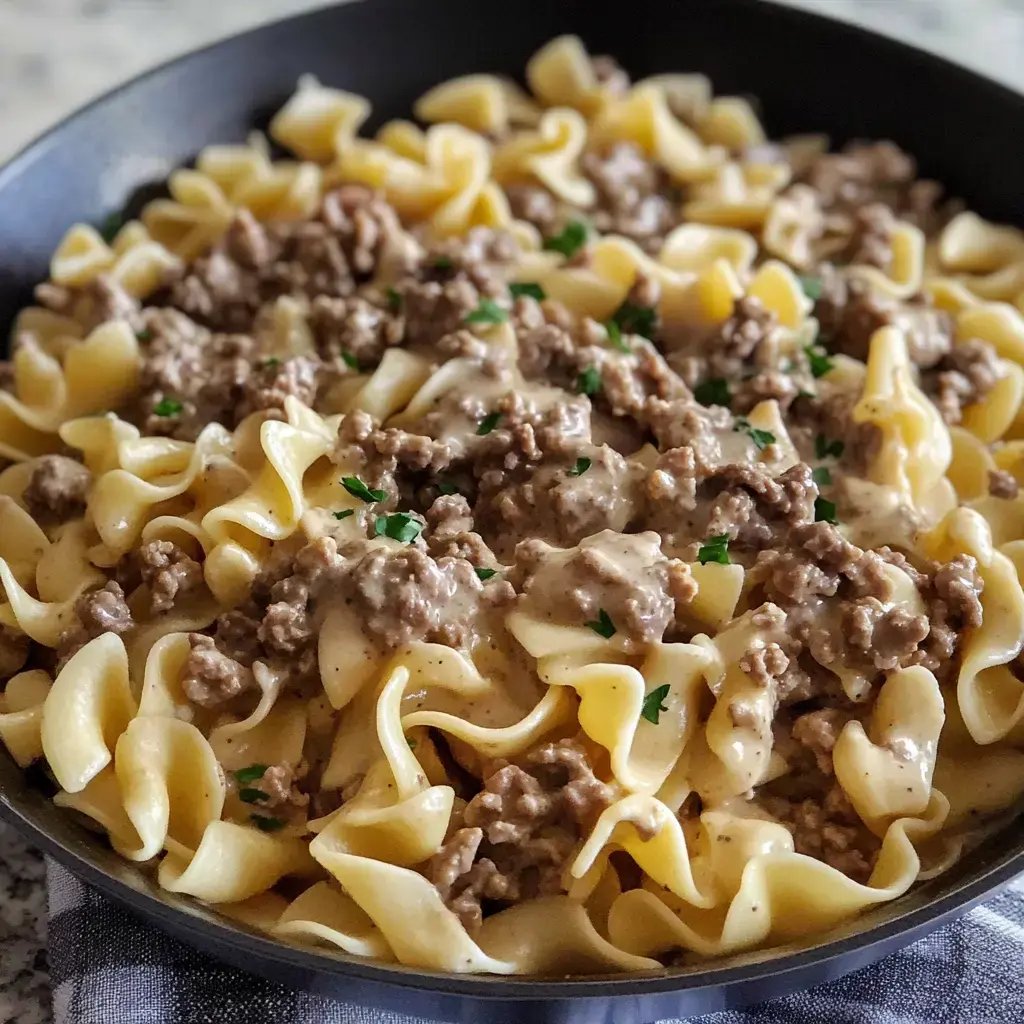 Egg noodles in a pan covered with ground beef in a rich creamy sauce and fresh parsley.