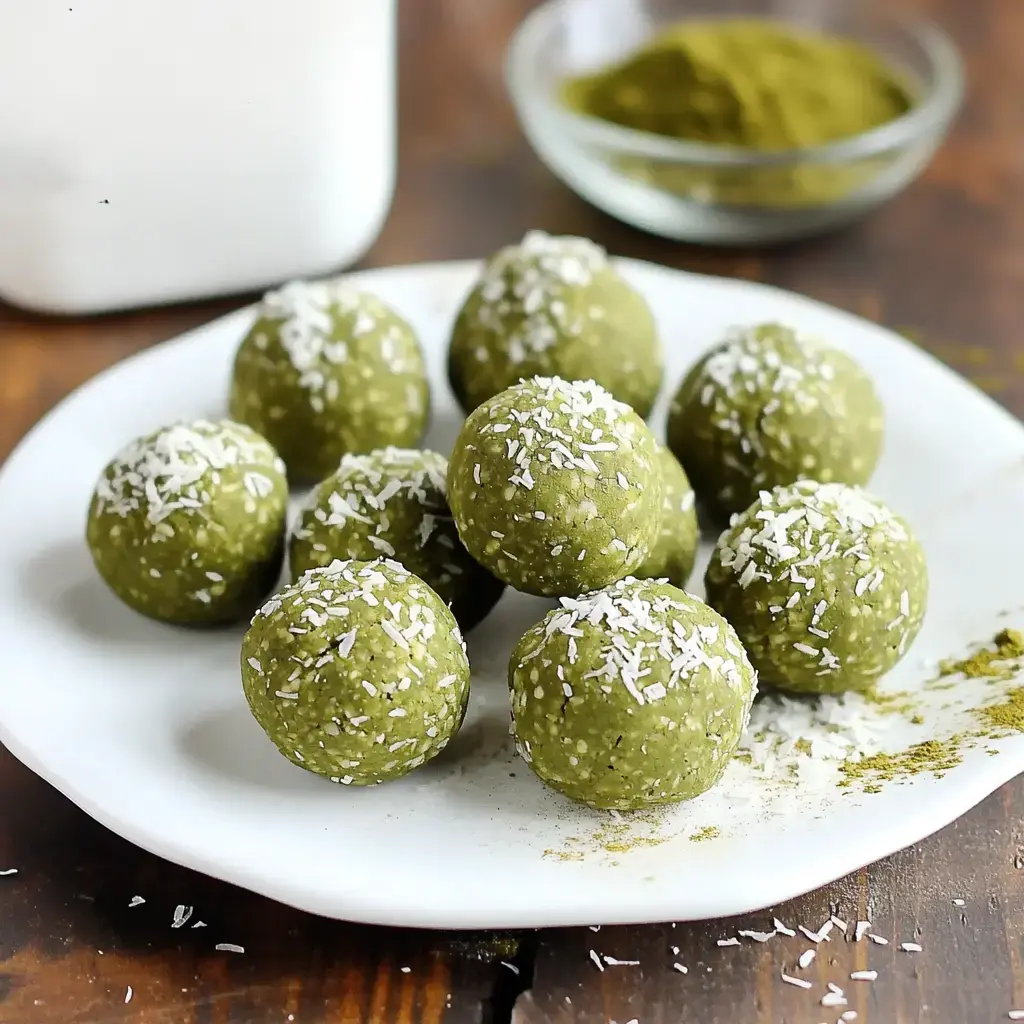 Green coconut-covered balls arranged on a plate, with a dusting of green powder and extra coconut sprinkled behind them.