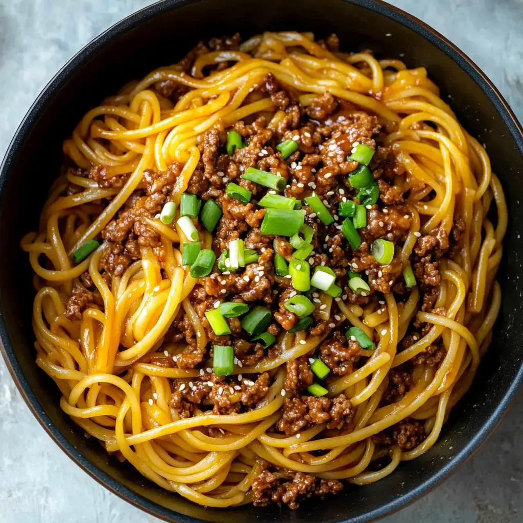 Spaghetti noodles covered in savory ground meat, fresh green onions, and sesame seeds sitting in a bowl.