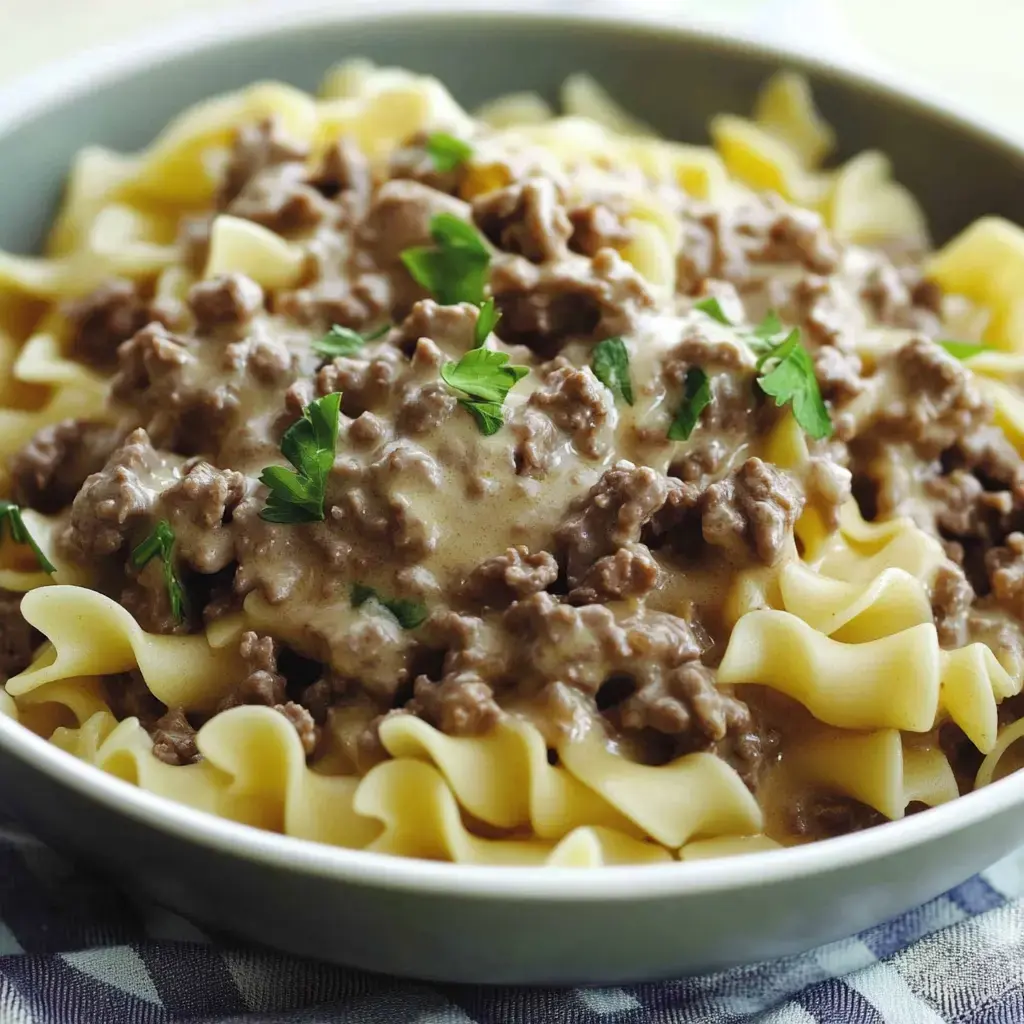 Egg noodles coated in creamy sauce with ground beef and sprinkled parsley, served in a bowl.