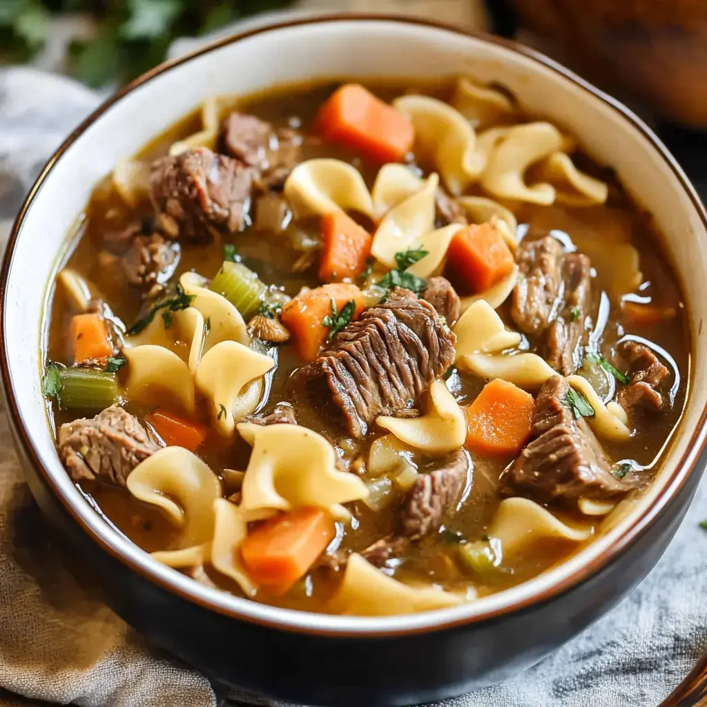 Steaming hot beef and noodle bowl with chunky beef, carrots, celery, and thick noodles swimming in a savory broth.