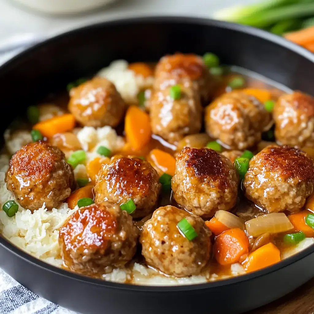 A bowl packed with saucy meatballs, carrots, onions, and a sprinkle of green onions on fluffy cauliflower rice.