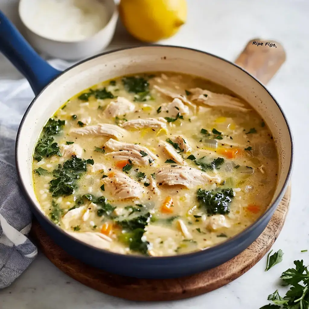 Chicken soup in a bowl set on a wooden table with shredded chicken, kale, bright veggies, a fresh lemon, and a little bowl of sauce.