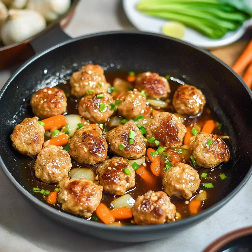 A pan of saucy meatballs with carrots and green onions scattered on top.