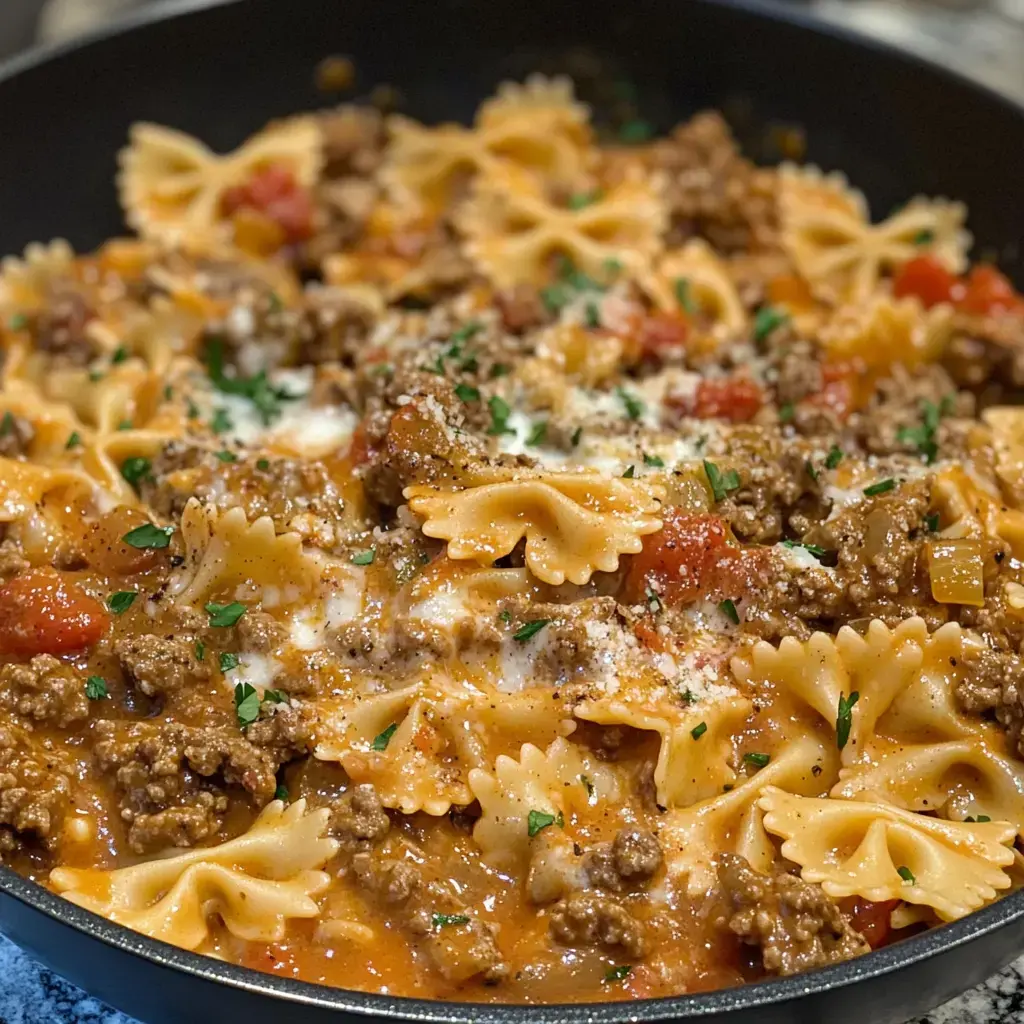 A pan loaded with bowties, beef, bits of tomato, gooey cheese, and fresh herbs ready to dig in.